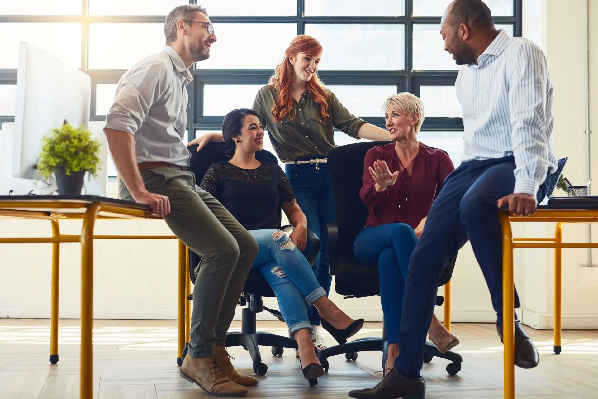 group of men and women sitting on chairs and desks in an office