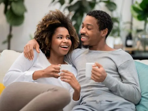 man and woman on couch smiling and drinking coffee