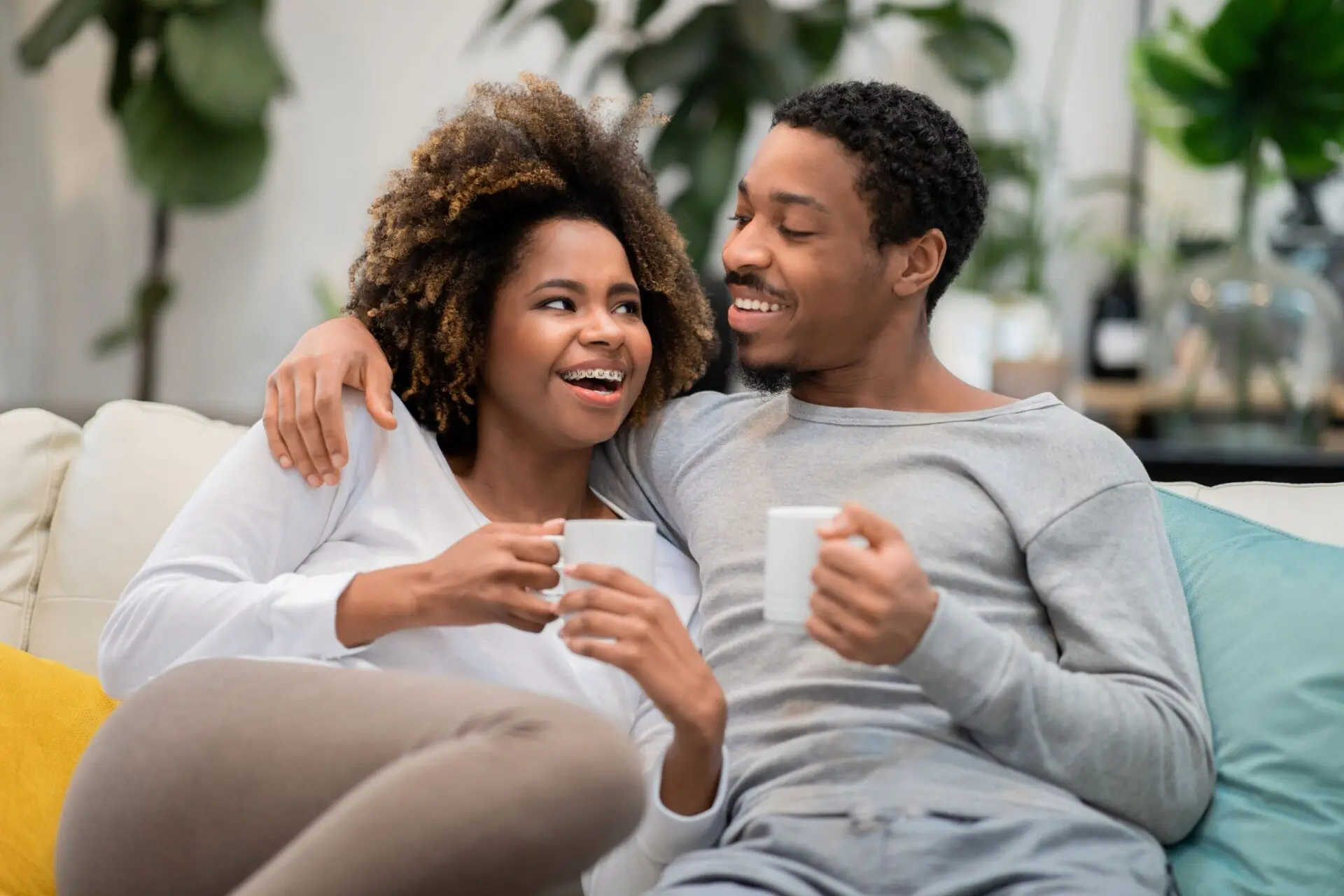 man and woman on couch smiling and drinking coffee