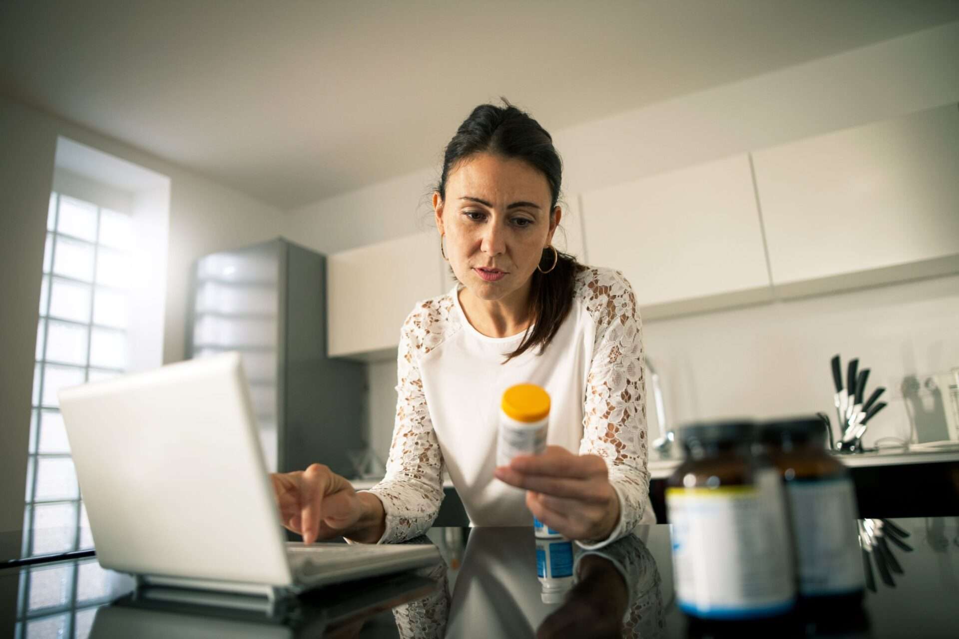 Woman reading pill bottle in front of computer