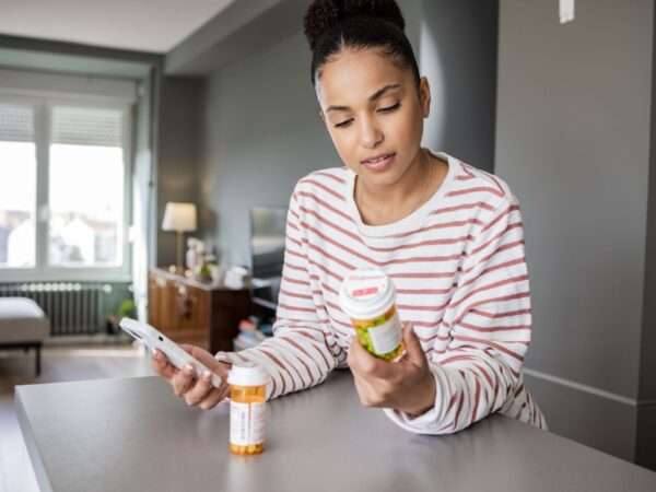 Woman holding phone and reading pill bottle