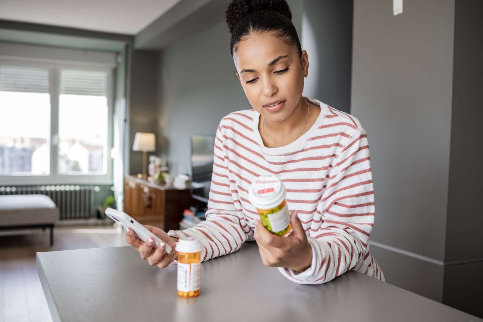 Woman holding phone and reading pill bottle