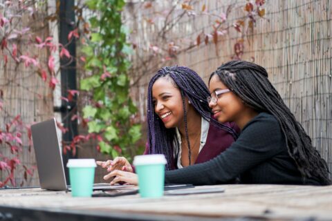 two friends with coffee cups working on a laptop