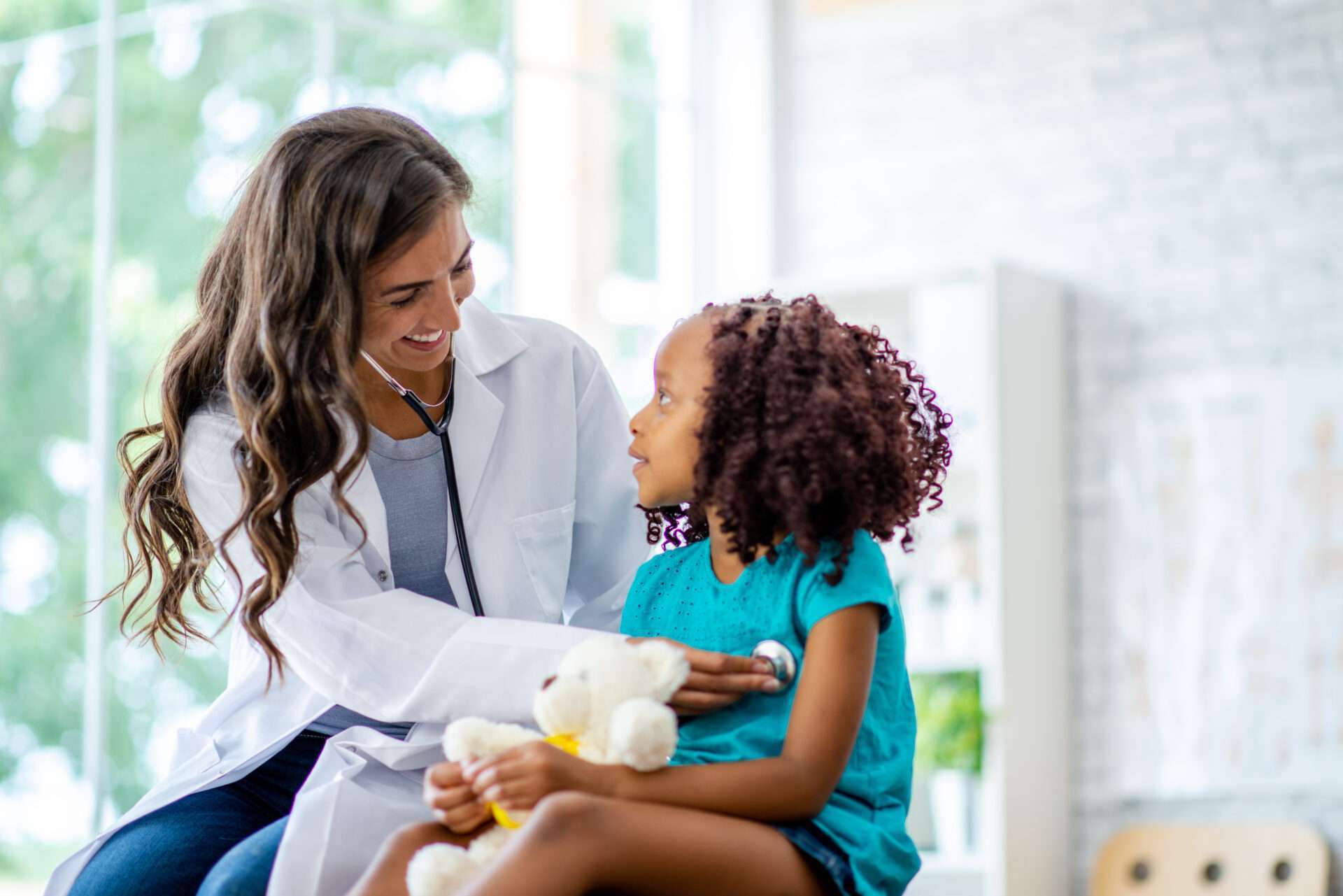 Doctor giving a child with teddy bear a check up